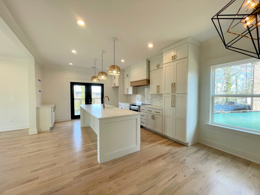 Example of a mid-sized transitional single-wall eat-in kitchen design with a farmhouse sink, shaker cabinets, white cabinets, quartz countertops, white backsplash, marble backsplash, stainless steel appliances, an island and white countertops