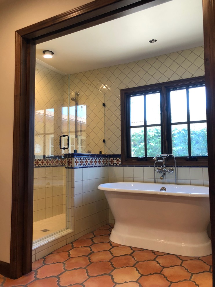 This is an example of a mid-sized mediterranean master bathroom in San Diego with raised-panel cabinets, dark wood cabinets, a freestanding tub, an alcove shower, beige walls, terra-cotta floors, an undermount sink, solid surface benchtops, red floor, a hinged shower door and beige benchtops.