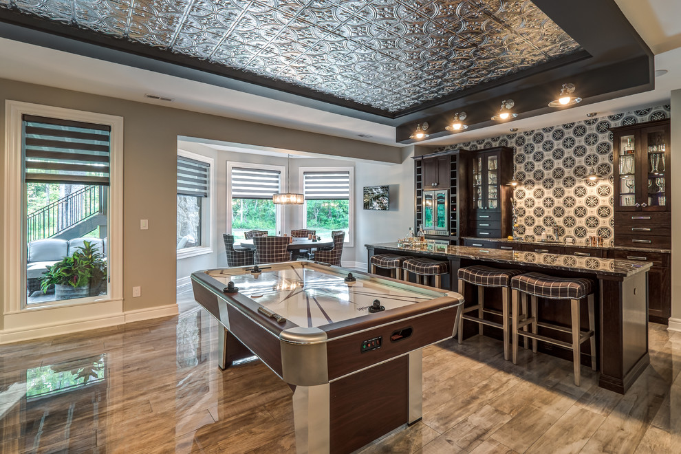 Expansive transitional open concept family room in Cincinnati with a home bar, grey walls, porcelain floors, no fireplace, a wall-mounted tv and brown floor.