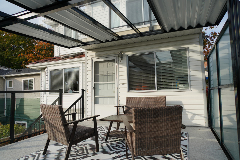 Diseño de terraza actual de tamaño medio en patio trasero con toldo y barandilla de vidrio