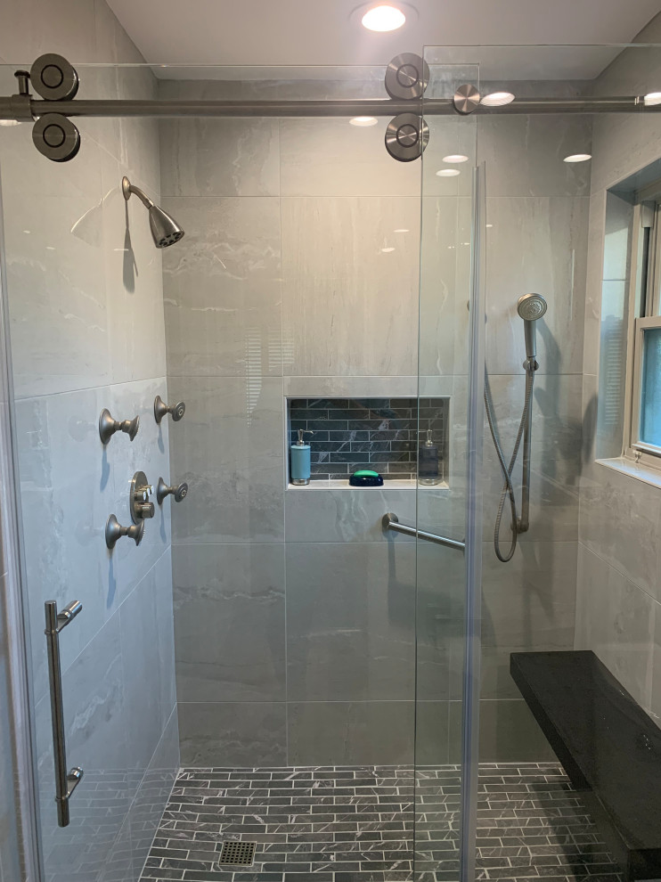 Photo of a mid-sized transitional master bathroom in Austin with a curbless shower, gray tile, porcelain tile, grey walls, porcelain floors, brown floor, a sliding shower screen, a shower seat, a built-in vanity and decorative wall panelling.