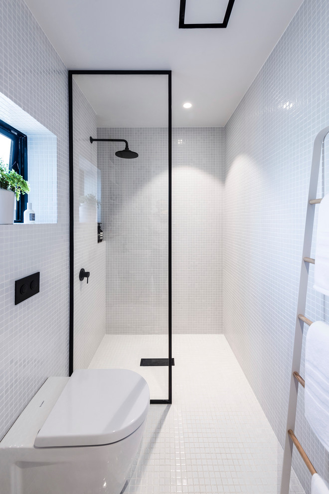 This is an example of a small contemporary master wet room bathroom in Christchurch with recessed-panel cabinets, light wood cabinets, a wall-mount toilet, white tile, mosaic tile, white walls, mosaic tile floors and a wall-mount sink.