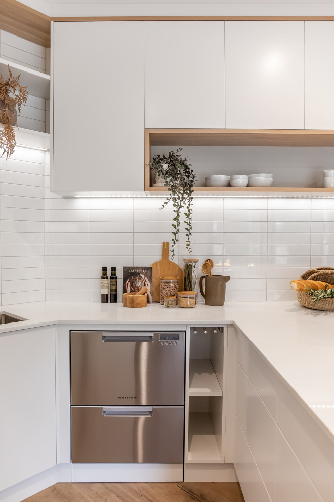 Small contemporary u-shaped kitchen/diner in Adelaide with a submerged sink, flat-panel cabinets, white cabinets, engineered stone countertops, white splashback, metro tiled splashback, stainless steel appliances, laminate floors, a breakfast bar, brown floors and white worktops.