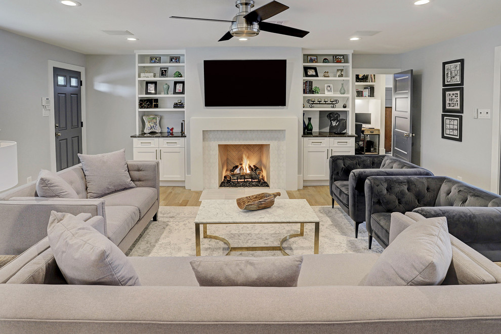 This is an example of a mid-sized transitional enclosed living room in Houston with grey walls, light hardwood floors, a standard fireplace, a wall-mounted tv and beige floor.