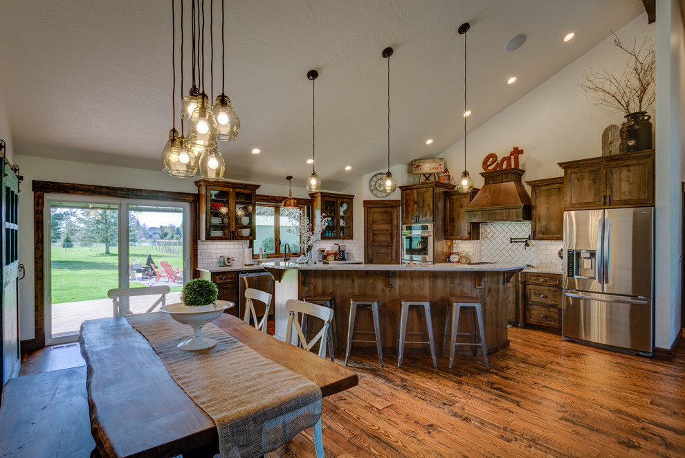 Example of a mid-sized mountain style u-shaped medium tone wood floor kitchen design in Seattle with a farmhouse sink, shaker cabinets, medium tone wood cabinets, quartzite countertops, white backsplash, subway tile backsplash, stainless steel appliances and an island