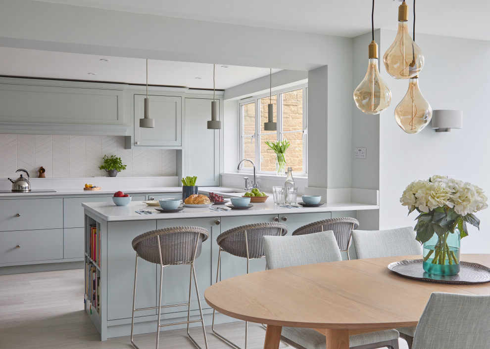 Design ideas for a mid-sized transitional u-shaped eat-in kitchen in Gloucestershire with an integrated sink, shaker cabinets, blue cabinets, quartzite benchtops, white splashback, ceramic splashback, black appliances, vinyl floors, a peninsula, grey floor and white benchtop.