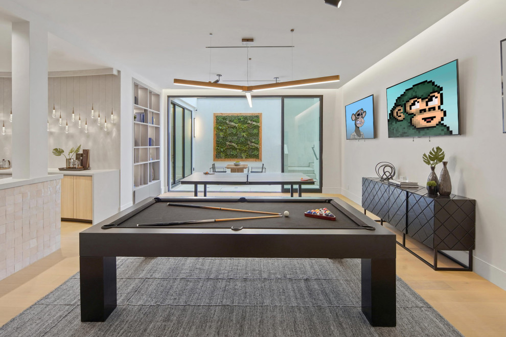 This is an example of a large contemporary walk-out basement in Los Angeles with a game room, white walls, light hardwood floors and beige floor.