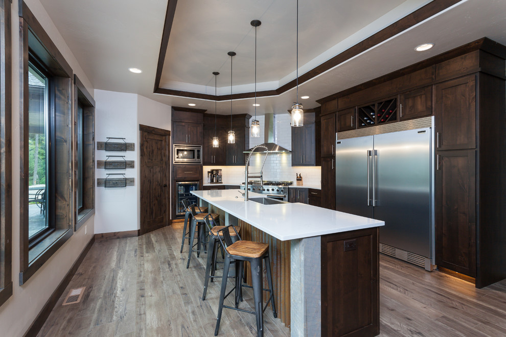 Mountain style kitchen photo with a farmhouse sink, white backsplash, ceramic backsplash, stainless steel appliances and an island