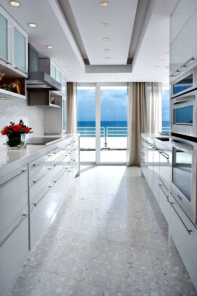 Design ideas for a contemporary galley kitchen in Miami with an undermount sink, flat-panel cabinets, white cabinets, white splashback, stainless steel appliances, beige floor and white benchtop.