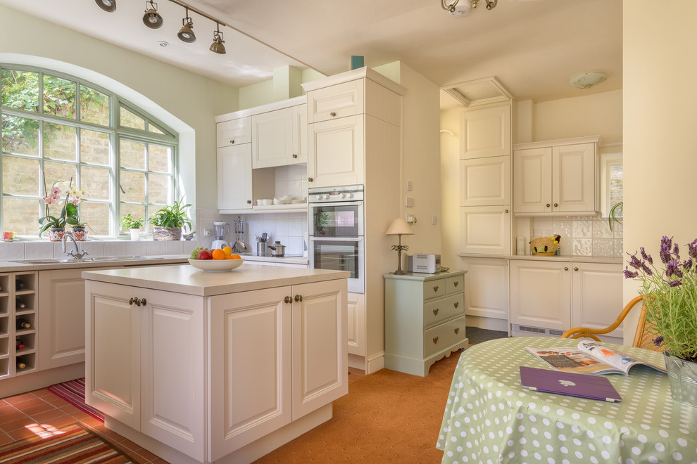 Mid-sized traditional u-shaped separate kitchen in Devon with a drop-in sink, recessed-panel cabinets, white cabinets, terra-cotta floors and with island.