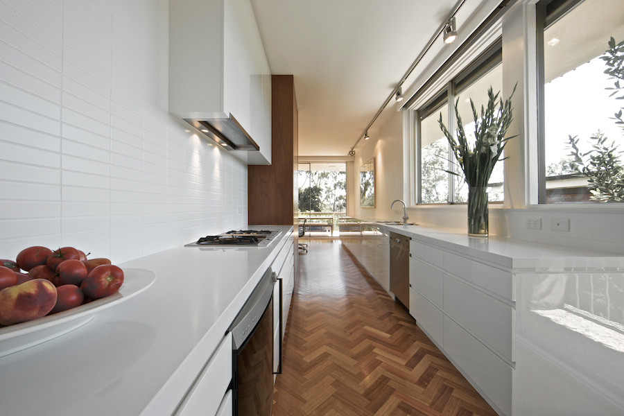 This is an example of a contemporary galley kitchen in Melbourne with flat-panel cabinets, white cabinets, quartz benchtops, white splashback, ceramic splashback, medium hardwood floors and no island.