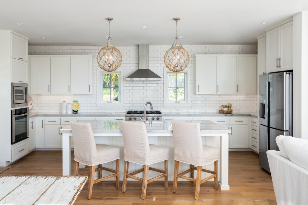 Inspiration for a beach style u-shaped open plan kitchen in San Diego with an undermount sink, shaker cabinets, white cabinets, white splashback, subway tile splashback, stainless steel appliances, medium hardwood floors, with island, brown floor and white benchtop.