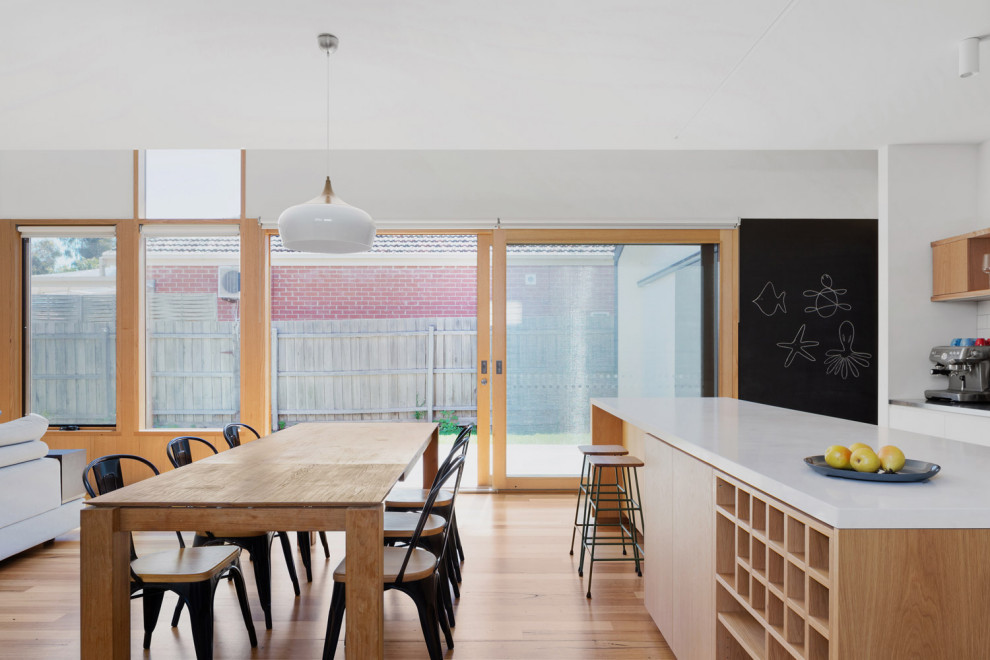 Photo of a mid-sized contemporary galley open plan kitchen in Melbourne with a drop-in sink, shaker cabinets, light wood cabinets, solid surface benchtops, white splashback, subway tile splashback, white appliances, light hardwood floors, with island and white benchtop.