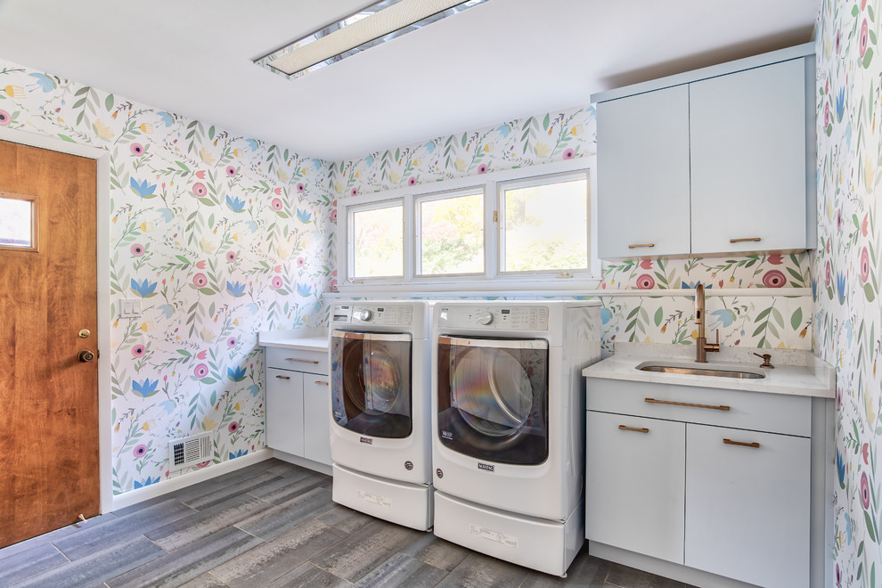 Inspiration for a large transitional single-wall laundry room in New York with flat-panel cabinets, multi-coloured walls, porcelain floors, a side-by-side washer and dryer, grey floor, white benchtop, an undermount sink and grey cabinets.