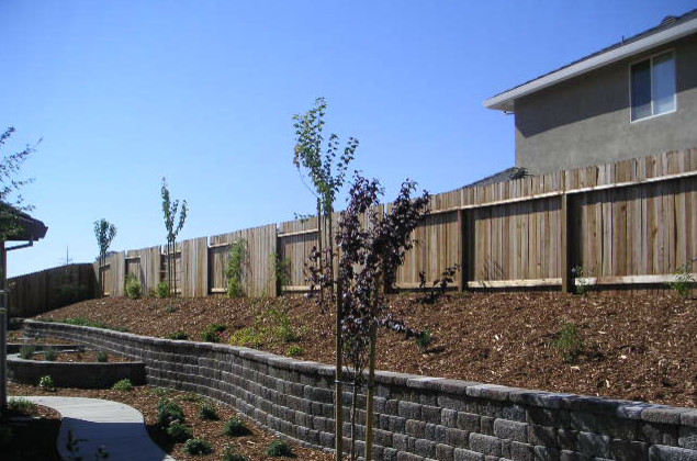 This is an example of a mid-sized backyard partial sun garden in Sacramento with a retaining wall and concrete pavers.