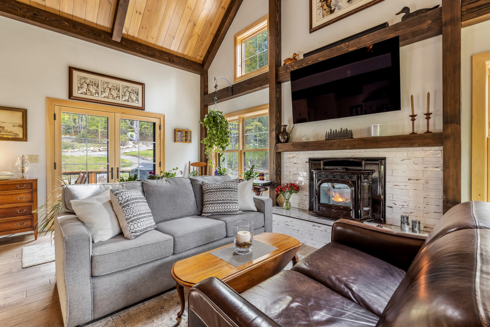 Inspiration for a country living room in Burlington with white walls, medium hardwood floors, a standard fireplace, a wall-mounted tv, brown floor, exposed beam, vaulted and wood.