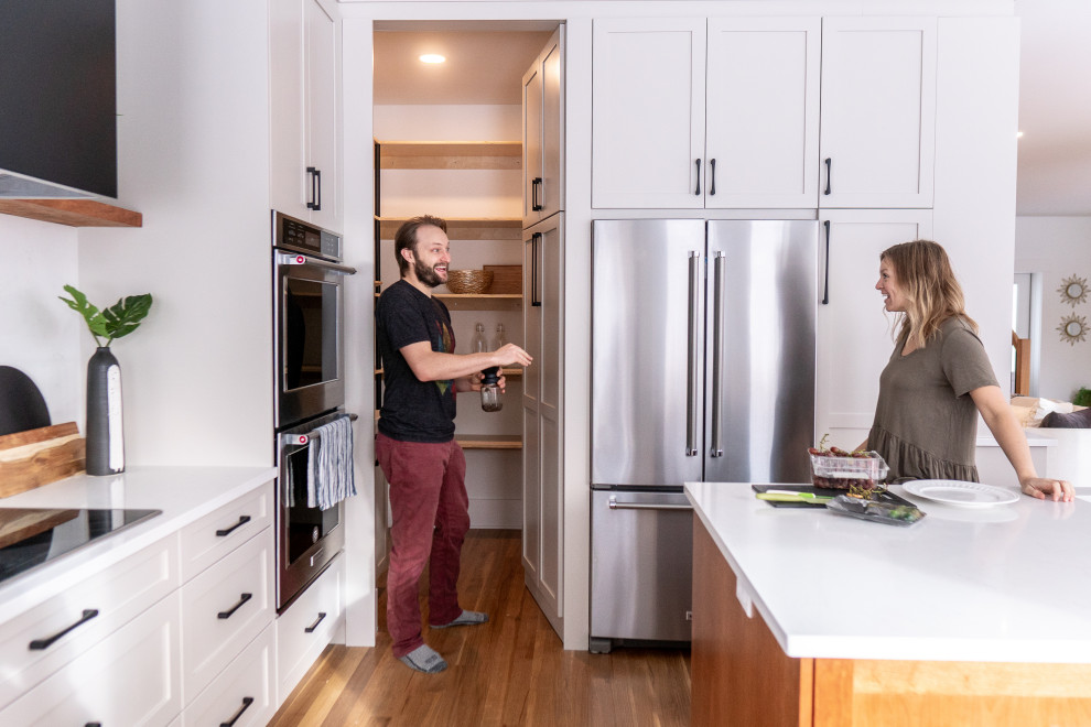 Eat-in kitchen - large transitional l-shaped medium tone wood floor and multicolored floor eat-in kitchen idea with shaker cabinets, white cabinets, quartz countertops, white backsplash, stone slab backsplash, stainless steel appliances, an island and white countertops