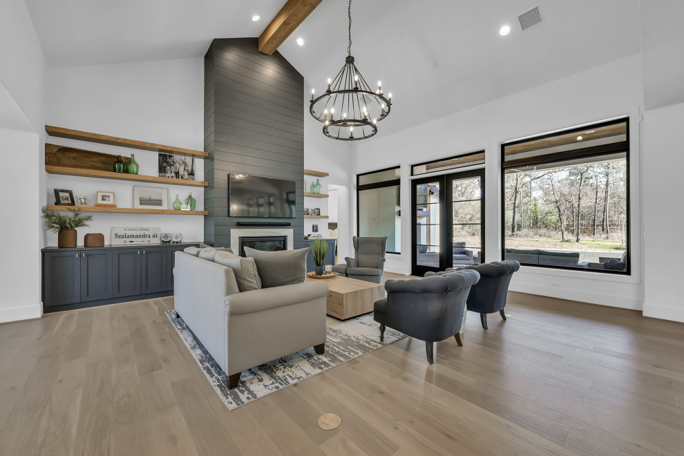 Inspiration for a large transitional open concept medium tone wood floor, brown floor and vaulted ceiling family room remodel in Houston with white walls, a standard fireplace, a shiplap fireplace and a wall-mounted tv