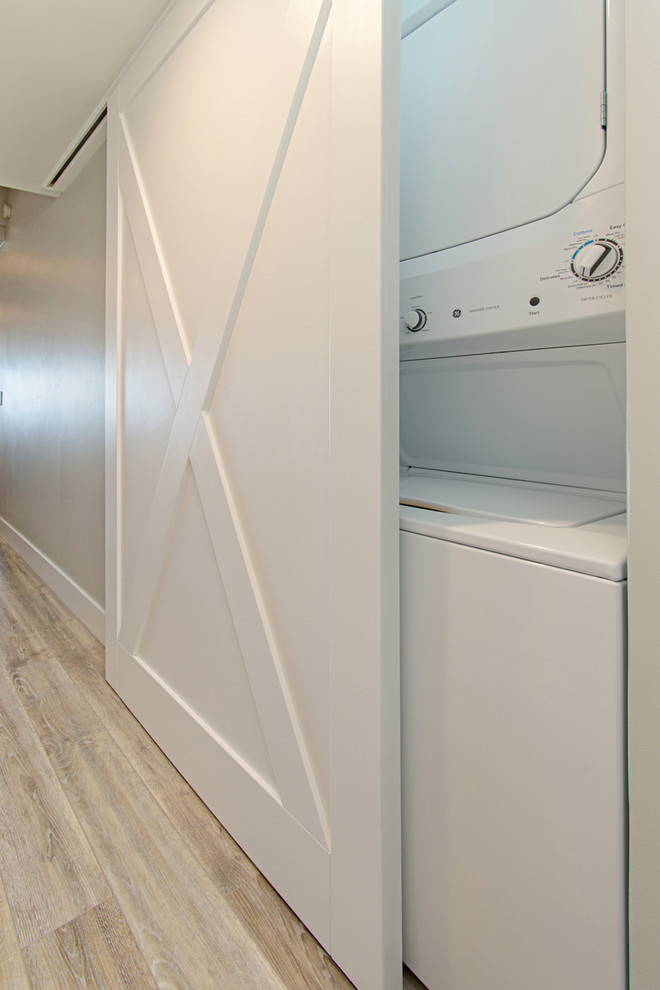 Photo of a mid-sized beach style single-wall laundry cupboard in San Diego with shaker cabinets, light wood cabinets, quartzite benchtops, green walls, vinyl floors, a stacked washer and dryer, grey floor and green benchtop.