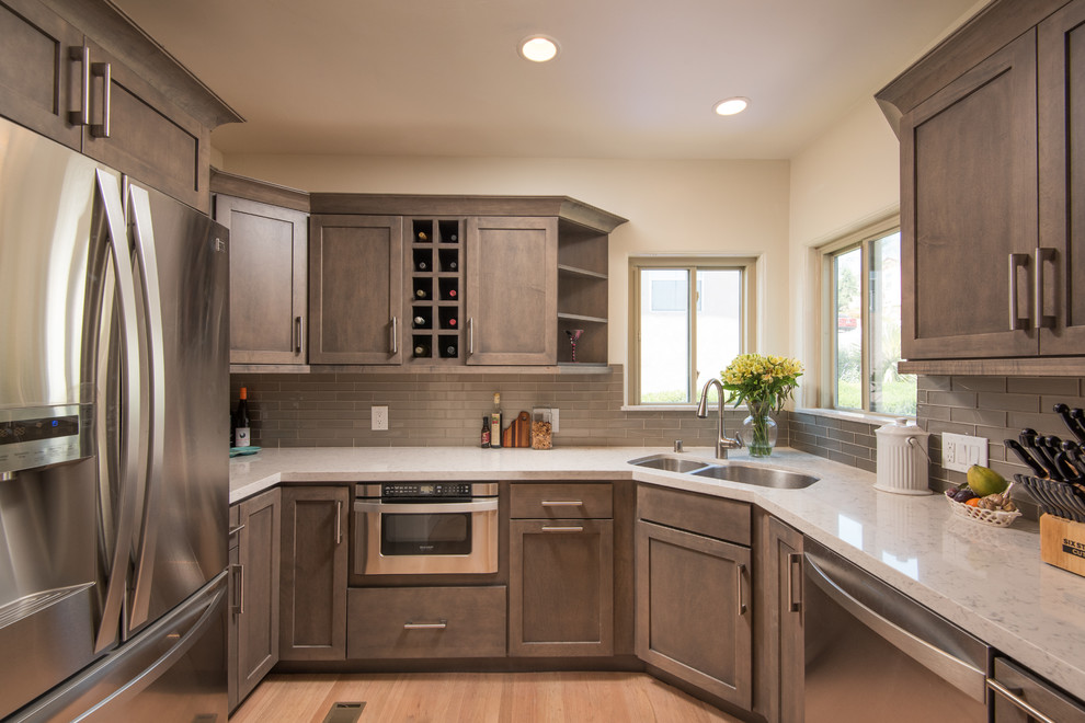 This is an example of a mid-sized transitional kitchen in San Diego with a double-bowl sink, shaker cabinets, quartz benchtops, grey splashback, glass tile splashback, stainless steel appliances and light hardwood floors.