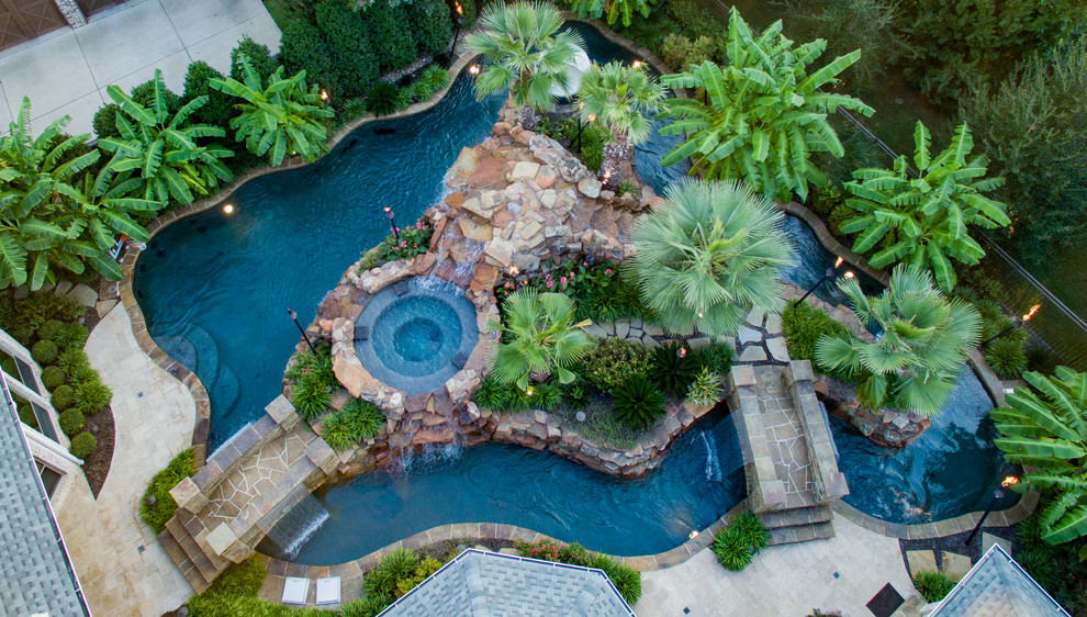 Inspiration for a large tropical backyard custom-shaped pool in Dallas with a water feature and natural stone pavers.