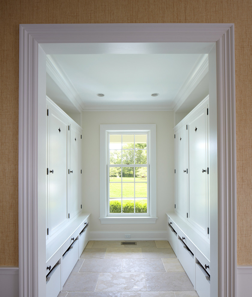 Large beach style gender-neutral walk-in wardrobe in New York with recessed-panel cabinets, white cabinets and limestone floors.
