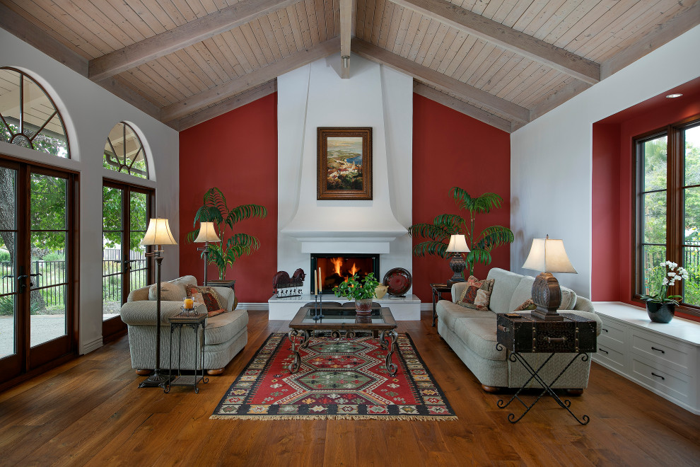 Example of a large tuscan formal and open concept brown floor, vaulted ceiling and medium tone wood floor living room design in Santa Barbara with white walls, a standard fireplace, a plaster fireplace and no tv