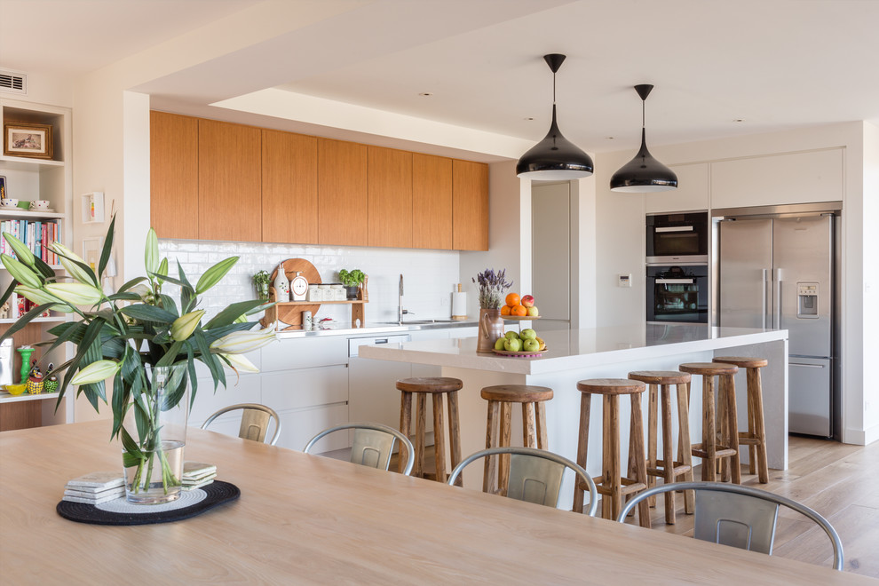 Contemporary l-shaped eat-in kitchen in Sydney with medium wood cabinets, white splashback, with island, white benchtop, flat-panel cabinets, subway tile splashback, stainless steel appliances, light hardwood floors and beige floor.
