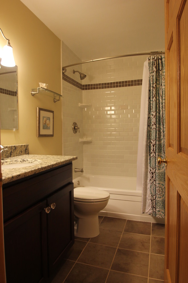 Photo of a mid-sized traditional bathroom in Cleveland with shaker cabinets, dark wood cabinets, an alcove tub, a shower/bathtub combo, white tile, subway tile, beige walls, an undermount sink, granite benchtops, ceramic floors, brown floor and a shower curtain.