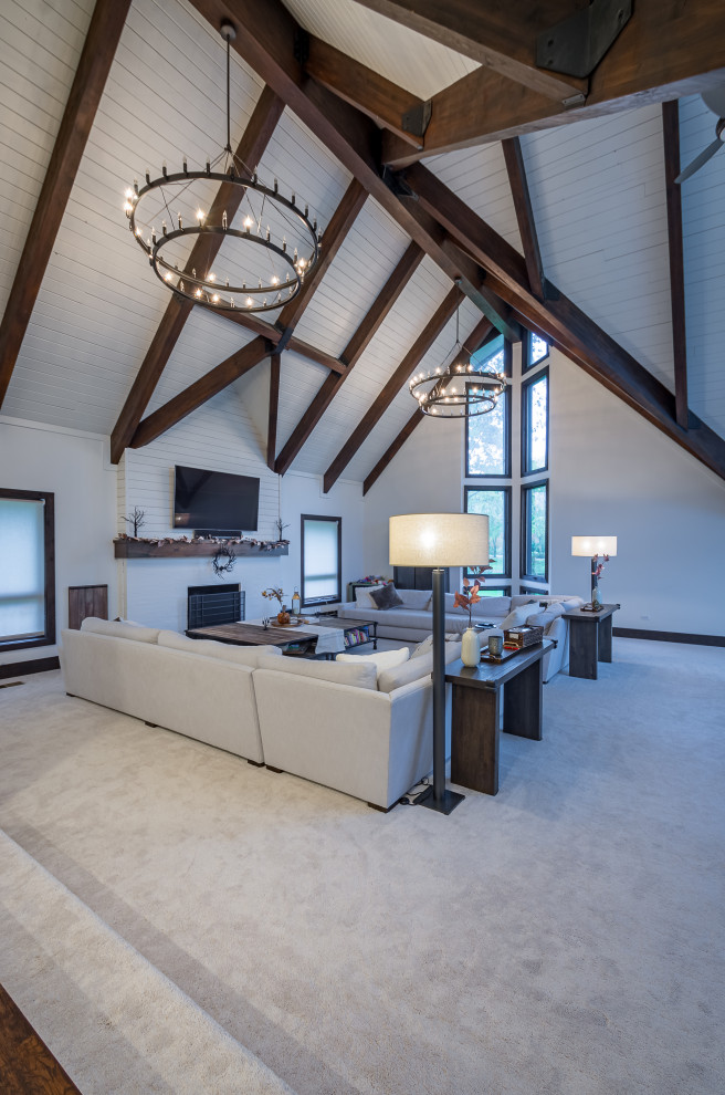 This is an example of an expansive farmhouse open plan games room in Chicago with a home bar, white walls, carpet, a standard fireplace, a wooden fireplace surround, a wall mounted tv, white floors, exposed beams, tongue and groove walls and a feature wall.