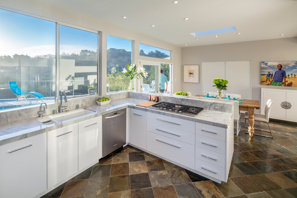This is an example of a large contemporary u-shaped eat-in kitchen in Los Angeles with an undermount sink, flat-panel cabinets, white cabinets, stainless steel appliances, a peninsula, marble benchtops, window splashback and slate floors.