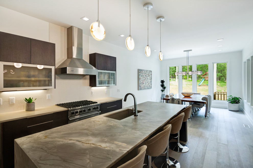 Photo of a large modern galley eat-in kitchen in Raleigh with an undermount sink, flat-panel cabinets, brown cabinets, granite benchtops, white splashback, ceramic splashback, stainless steel appliances, light hardwood floors, with island, grey floor and green benchtop.