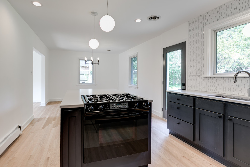 Mid-sized midcentury l-shaped open plan kitchen in Richmond with raised-panel cabinets, black cabinets, white splashback, ceramic splashback, with island and white benchtop.