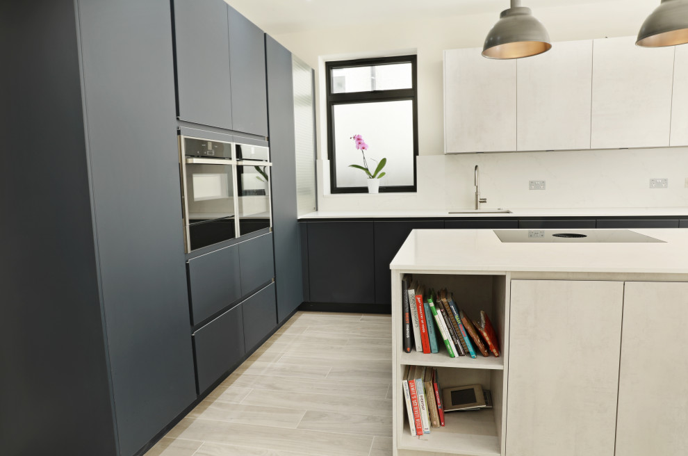 Large contemporary l-shaped kitchen/diner in London with a built-in sink, flat-panel cabinets, blue cabinets, quartz worktops, white splashback, stone slab splashback, black appliances, laminate floors, an island, white worktops and feature lighting.