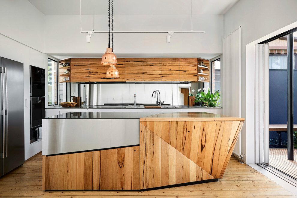 Design ideas for a contemporary l-shaped kitchen in Melbourne with an undermount sink, flat-panel cabinets, medium wood cabinets, mirror splashback, black appliances, light hardwood floors, with island and multi-coloured benchtop.