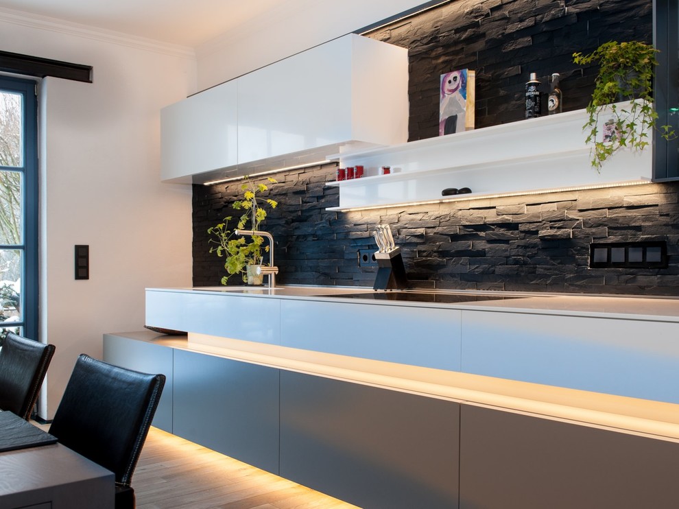 Photo of a contemporary single-wall eat-in kitchen in Other with flat-panel cabinets, black splashback, light hardwood floors, a single-bowl sink, white cabinets, stone tile splashback and no island.
