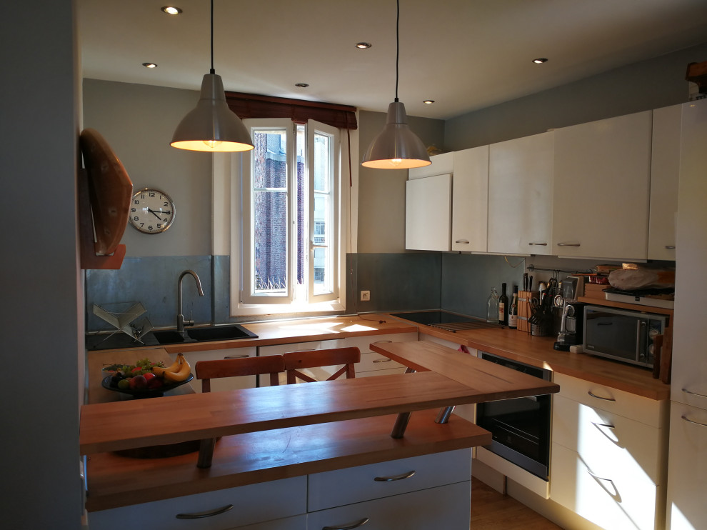 Bild på ett mellanstort funkis brun brunt kök, med en dubbel diskho, luckor med profilerade fronter, vita skåp, träbänkskiva, stänkskydd med metallisk yta, rostfria vitvaror, ljust trägolv, en köksö och beiget golv