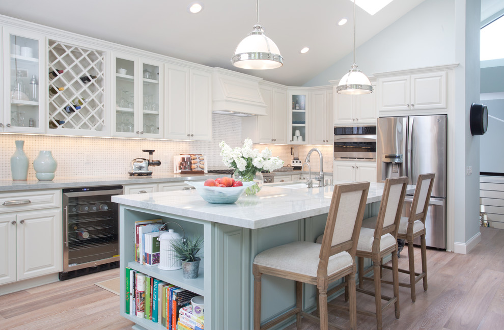 Inspiration for a beach style l-shaped kitchen in San Diego with raised-panel cabinets, white cabinets, white splashback, stainless steel appliances, light hardwood floors and with island.