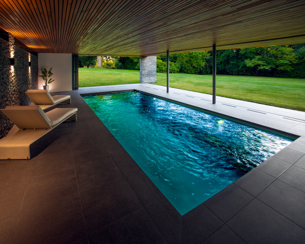 This is an example of a mid-sized modern backyard rectangular infinity pool in Kent with a pool house and tile.