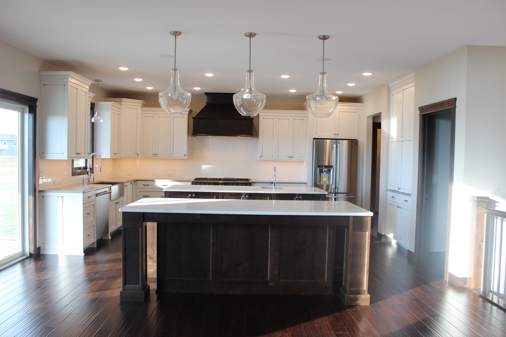 Inspiration for a large transitional l-shaped dark wood floor enclosed kitchen remodel with a farmhouse sink, shaker cabinets, white cabinets, quartz countertops, white backsplash, subway tile backsplash, stainless steel appliances and an island