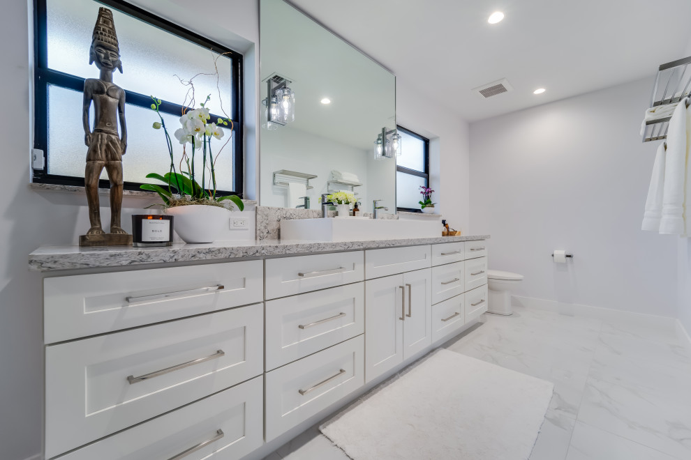 Photo of a large modern master bathroom in Miami with shaker cabinets, white cabinets, a double shower, a two-piece toilet, gray tile, stone slab, grey walls, ceramic floors, a trough sink, grey floor, a hinged shower door and grey benchtops.