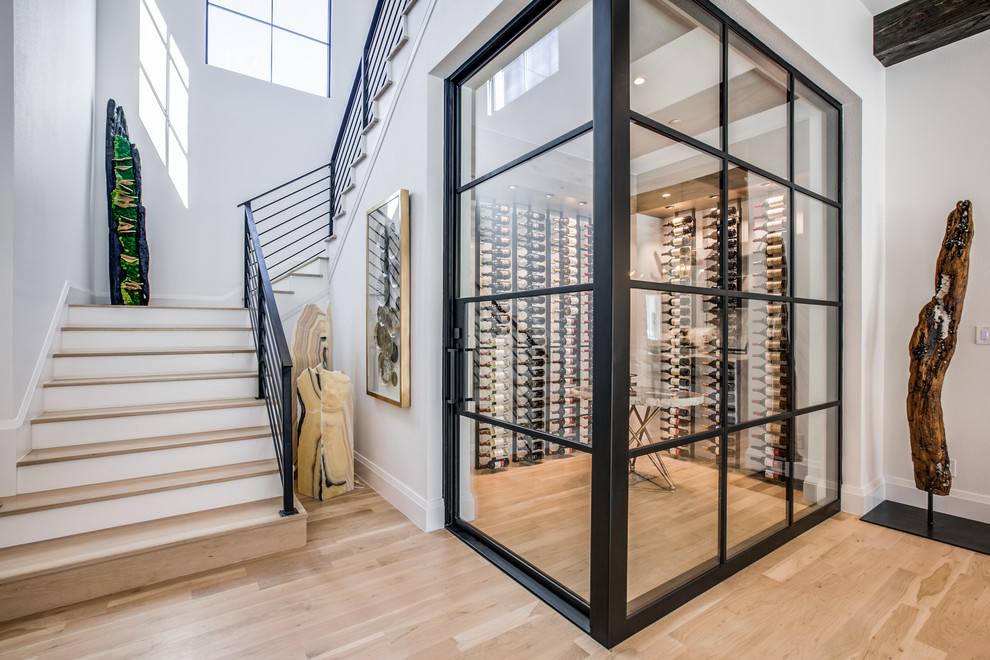 This is an example of a mid-sized mediterranean wine cellar in Dallas with light hardwood floors, display racks and brown floor.