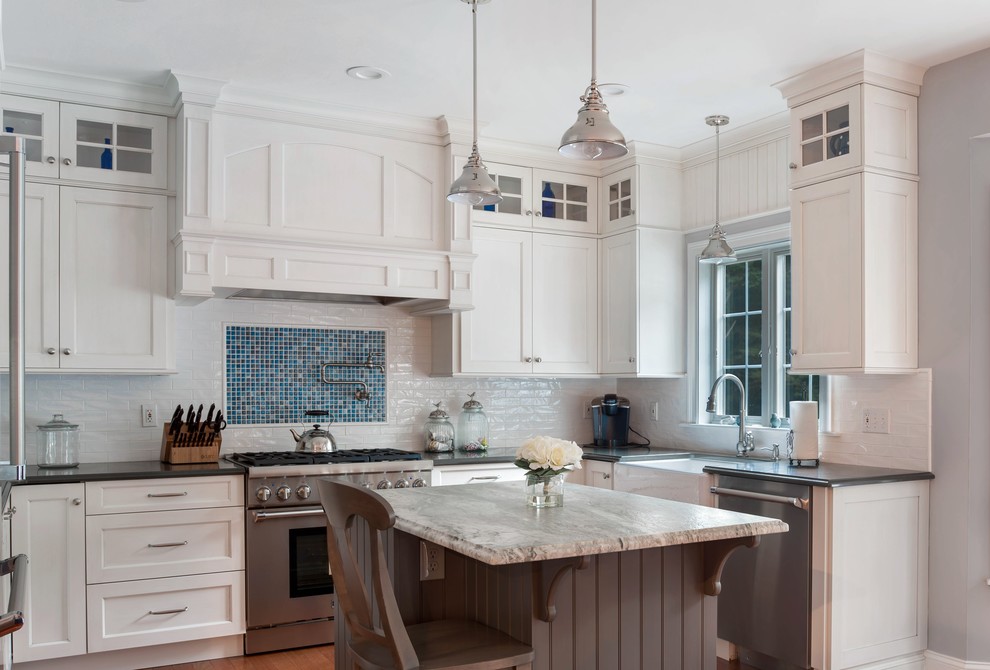Traditional u-shaped kitchen in Providence with a farmhouse sink, shaker cabinets, white cabinets, white splashback, subway tile splashback, stainless steel appliances, medium hardwood floors, with island, brown floor and black benchtop.