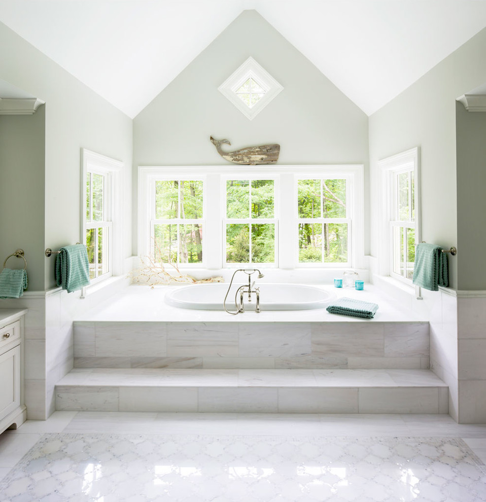 Photo of a large beach style master bathroom in New York with a drop-in tub, recessed-panel cabinets, white cabinets, white tile, stone tile, green walls, marble floors, an undermount sink and marble benchtops.