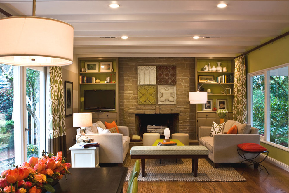 Photo of a traditional family room in San Francisco with green walls, medium hardwood floors, a standard fireplace, a stone fireplace surround, a wall-mounted tv and brown floor.