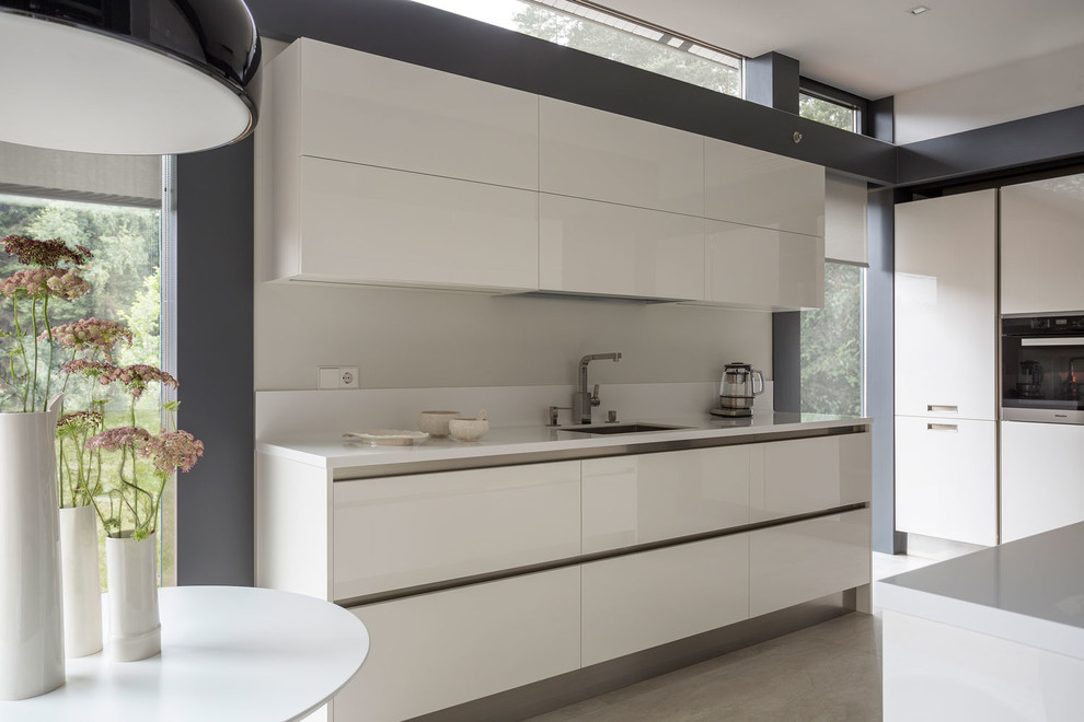 Inspiration for a mid-sized contemporary u-shaped separate kitchen in Moscow with an undermount sink, flat-panel cabinets, white cabinets, solid surface benchtops, white splashback, stainless steel appliances, porcelain floors and beige floor.