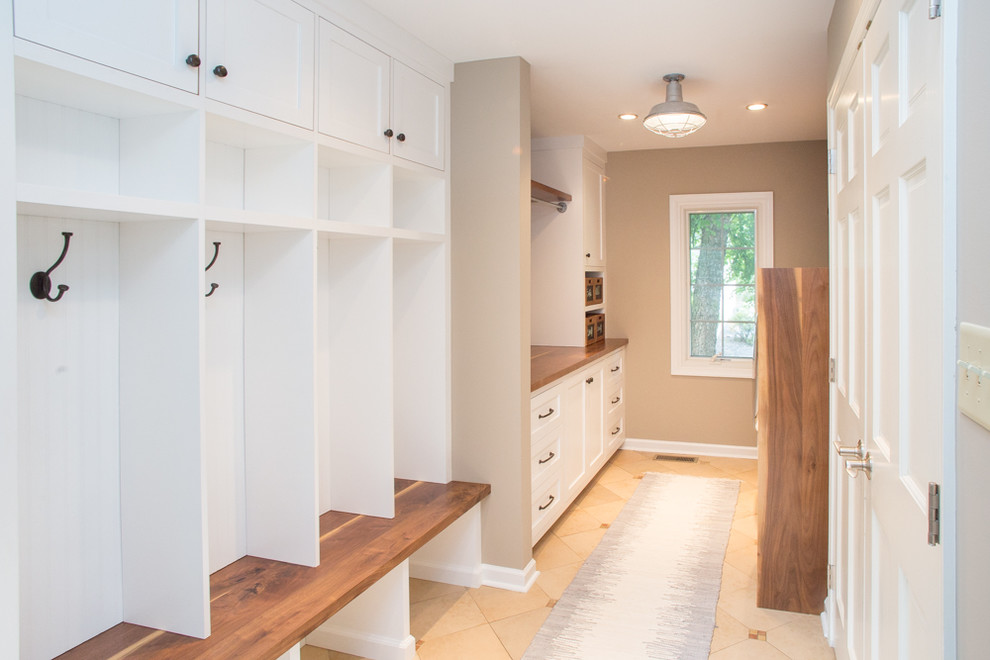 This is an example of a large transitional galley utility room in Philadelphia with shaker cabinets, white cabinets, wood benchtops, beige walls, ceramic floors and a side-by-side washer and dryer.