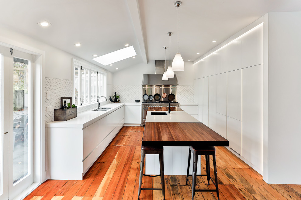 Photo of a contemporary l-shaped kitchen in Auckland with a double-bowl sink, flat-panel cabinets, white cabinets, white splashback, stainless steel appliances and with island.