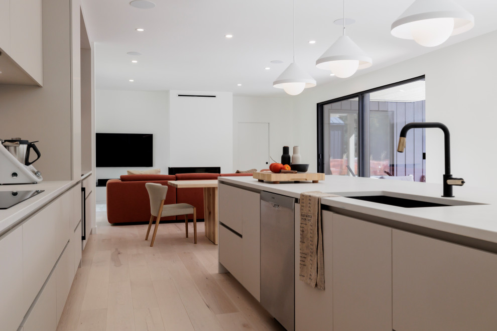 This is an example of a large scandinavian galley open plan kitchen in New York with an undermount sink, flat-panel cabinets, beige cabinets, quartz benchtops, beige splashback, engineered quartz splashback, stainless steel appliances, painted wood floors, with island and white benchtop.