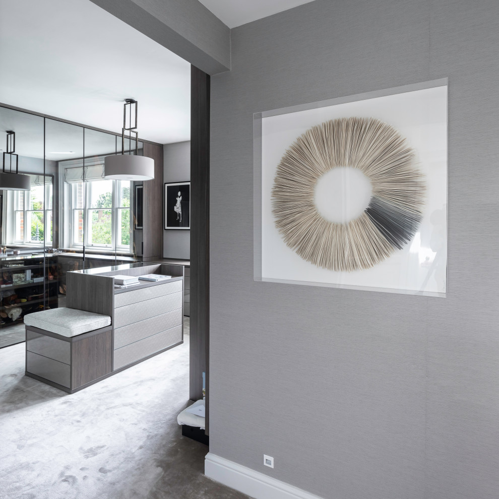Inspiration for a large contemporary gender-neutral dressing room in Hertfordshire with glass-front cabinets, dark wood cabinets, carpet and grey floor.